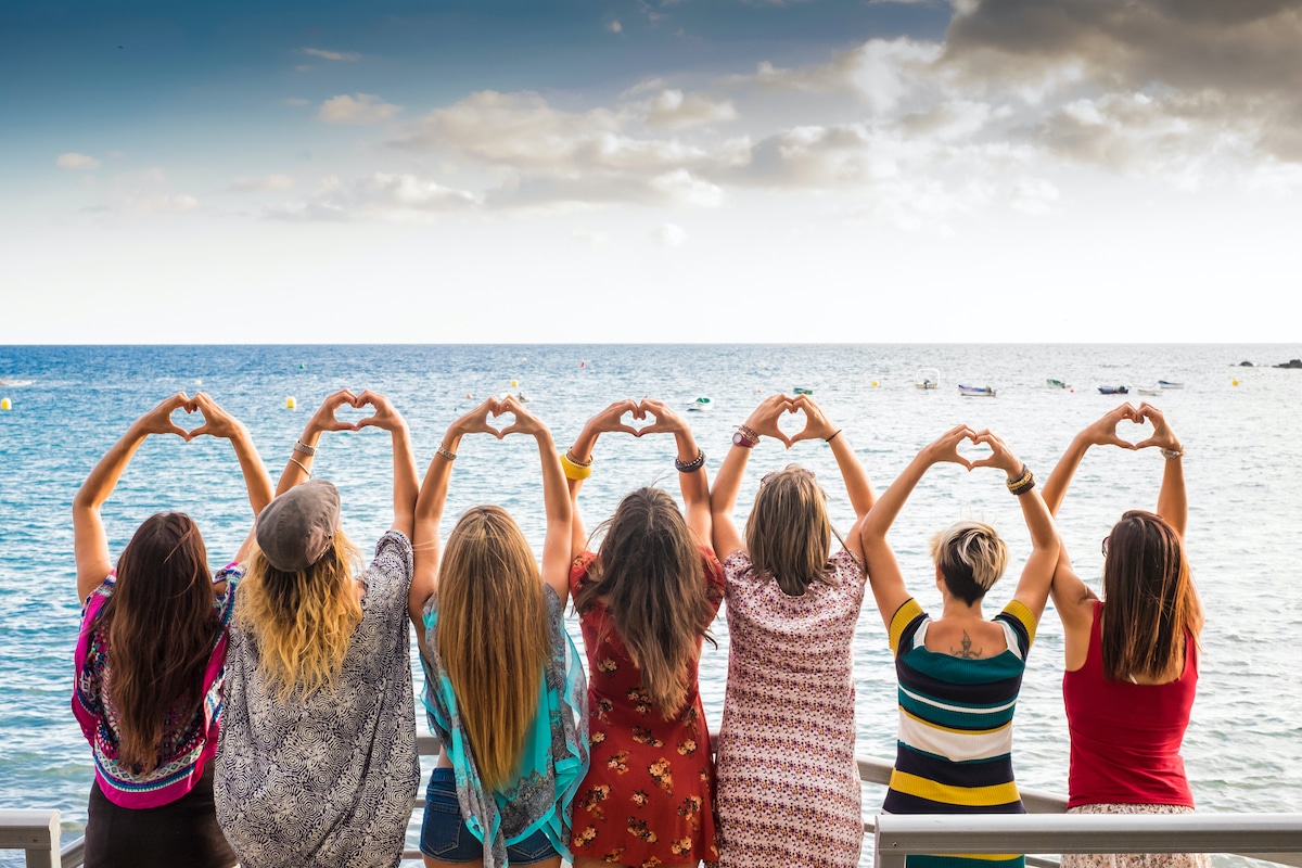 Group of girls making hearts with their hands in front of water scene