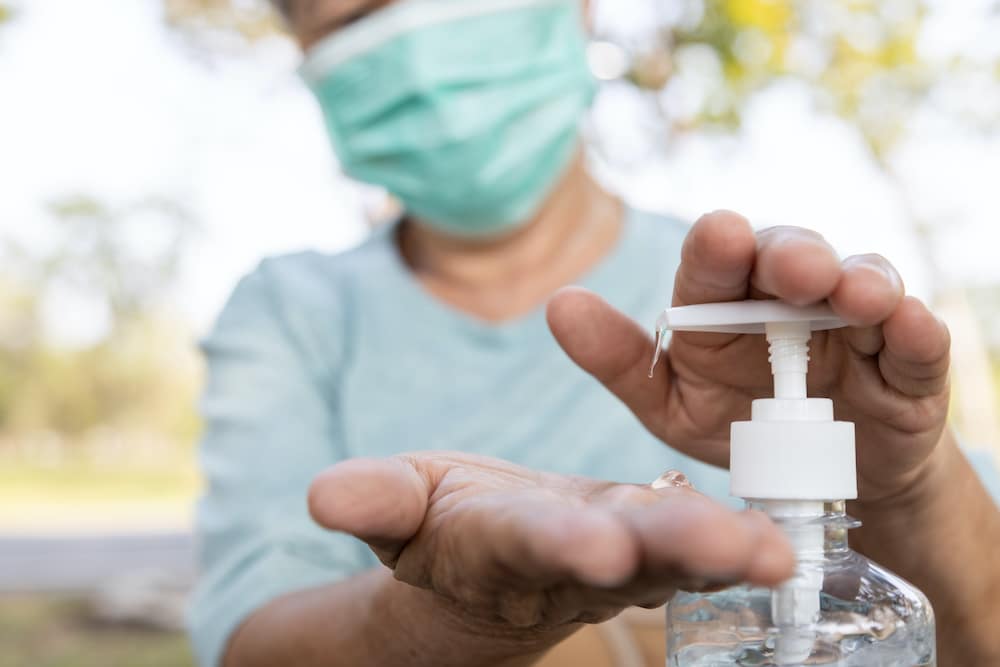 Elderly woman wearing a mask and using hand sanitizer for infection control